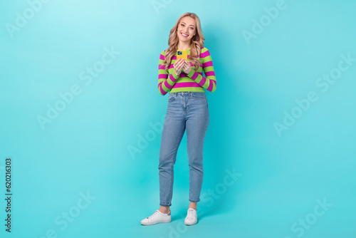 Full length photo of cheerful sweet lady wear striped pullover writing sms iphone samsung apple modern device isolated teal color background