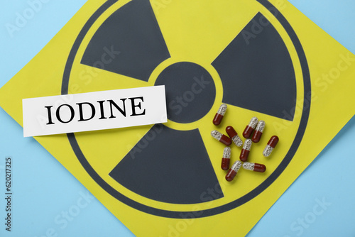 Paper note with word Iodine, pills and radiation sign on light blue background, top view photo