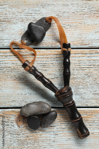 Black slingshot with stones on old light blue wooden table, flat lay