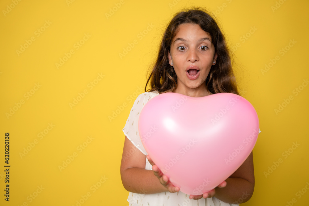 cheerful cute little lady receive birthday present hold heart shaped balloon isolated on yellow color background cheerful cute little lady receive birthday present hold heart shaped balloon isolated on yellow color background