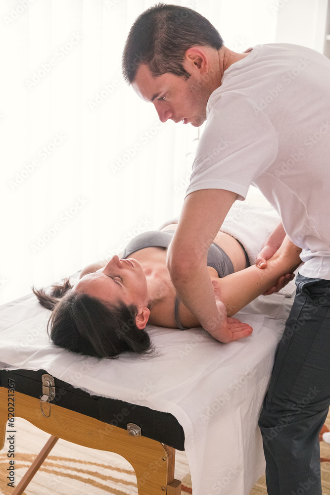 Therapist doing manipulation technique on the humerus. Young Caucasian woman being treated by therapist to help alleviate pain or improve physical condition.