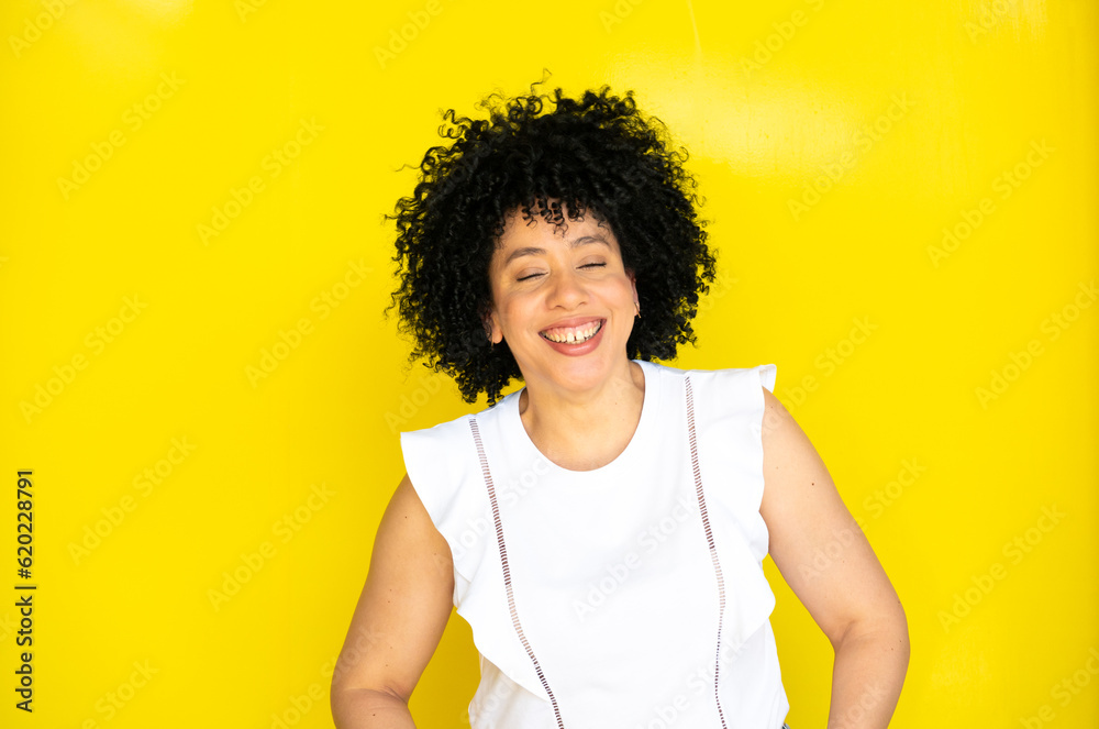 Cuban young woman with afro hair laughing with her eyes closed. Yellow background Cuban young woman with afro hair laughing with her eyes closed. Yellow background