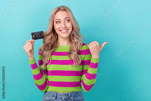 Photo of gorgeous woman dressed striped sweatshirt hold card indicating look at eshop ad empty space isolated on teal color background