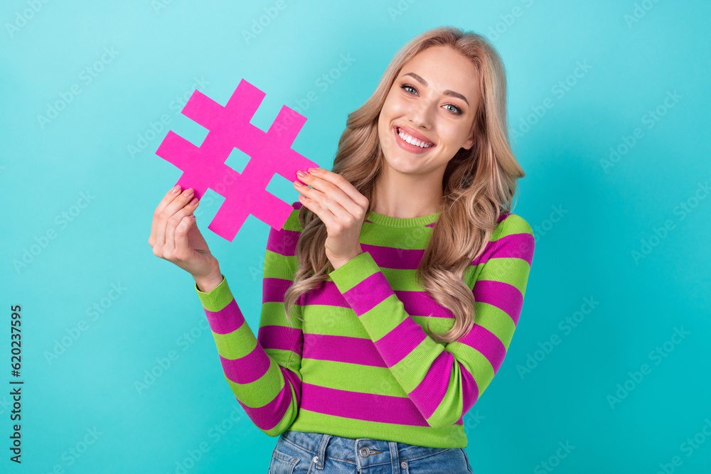 Photo portrait of pretty young girl hold pink hashtag smm manager dressed stylish striped outfit isolated on aquamarine color background Photo portrait of pretty young girl hold pink hashtag smm manager dressed stylish striped outfit isolated on aquamarine color background