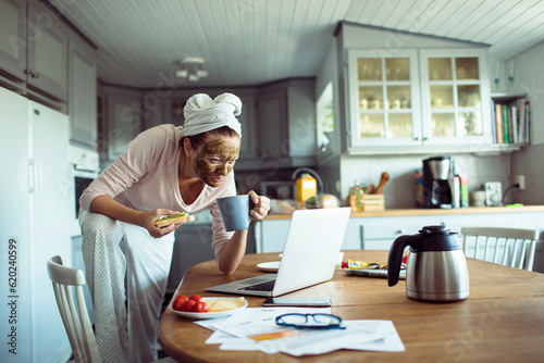 Young woman having breakfast in the morning and using a laptop in the kitchen © Geber86