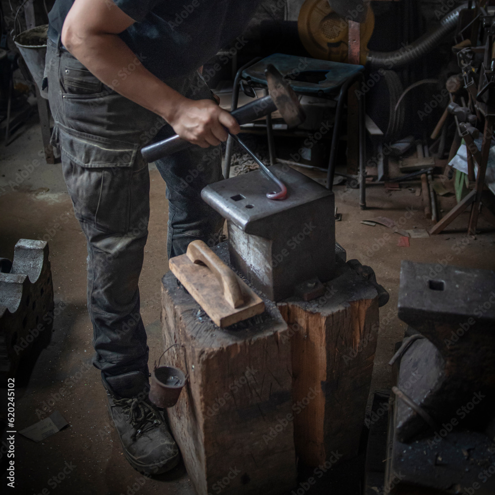 Man in a dark forge workshop forging red hot steel with a hammer on an iron anvil Man in a dark forge workshop forging red hot steel with a hammer on an iron anvil
