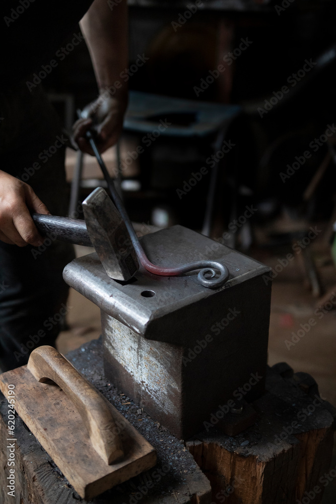 Man in a dark forge workshop forging red hot steel with a hammer on an iron anvil Man in a dark forge workshop forging red hot steel with a hammer on an iron anvil