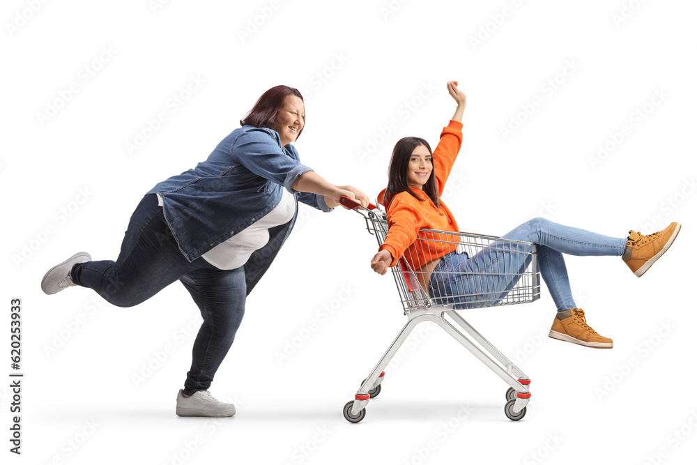 Full length profile shot of an overweight female pushing a friend inside a shopping cart