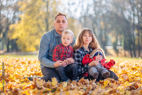 A young family sits in the park on a leafy, sunny autumn day.