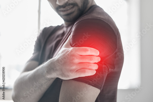 Hand, arm pain and injury with a man shoulder in red highlight during a fitness workout. Healthcare, medical and anatomy with a male athlete holding a joint after an accident or emergency in the gym