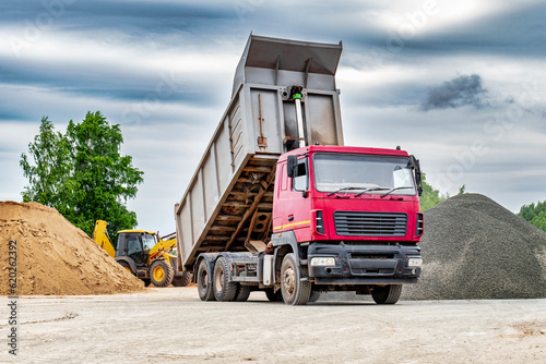 Dump truck with a raised body at a construction site. Transportation and unloading of sand or soil. Technique for transportation of bulk materials. Transportation of bulk building materials. photo