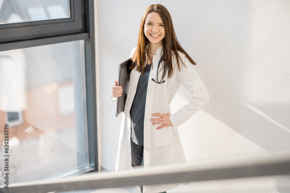 Portrait of a confident female doctor in medical gown walking with folder on staircase at modern clinic Portrait of a confident female doctor in medical gown walking with folder on staircase at modern clinic