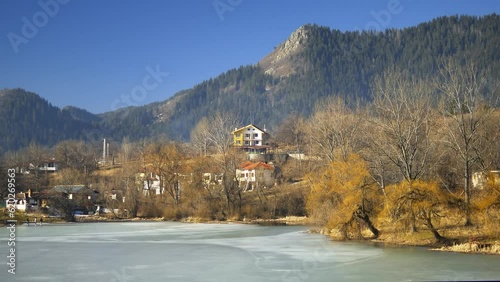 Beautiful lakeside village nestled among colorful trees displaying autumn foliage. Frozen pond with cottages in forest. A village at the Province of Plovdiv, Rhodope Mountains in Bulgaria
 photo