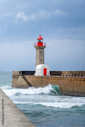 Waves crash against the rocky coastline. and front of Felgueiras Lighthouse. Foz of Douro, Portugal, Porto District.