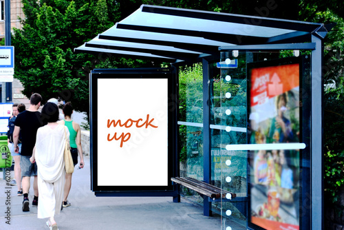 Fototapeta Naklejka Na Ścianę i Meble -  bus shelter with blank ad panel. billboard display. empty white lightbox sign at bus stop. billboard mockup. glass structure. city transit station. urban street. green setting. outdoor advertising.