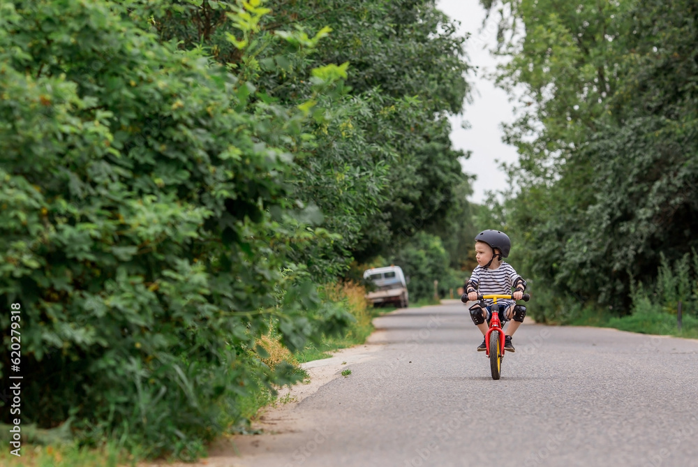 Fototapeta premium A cheerful little boy rides a running bike in a helmet outdoors. A happy child is engaged in an active sport. Protection. Life insurance and child safety.