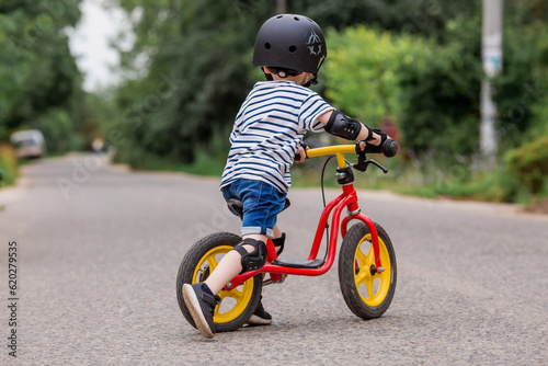 A cheerful little boy rides a running bike in a helmet outdoors. A happy child is engaged in an active sport. Protection. Life insurance and child safety.