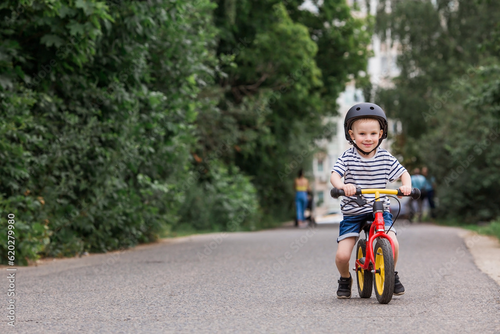 A cheerful little boy rides a running bike in a helmet outdoors. A happy child is engaged in an active sport. Protection. Life insurance and child safety. A cheerful little boy rides a running bike in a helmet outdoors. A happy child is engaged in an active sport. Protection. Life insurance and child safety.