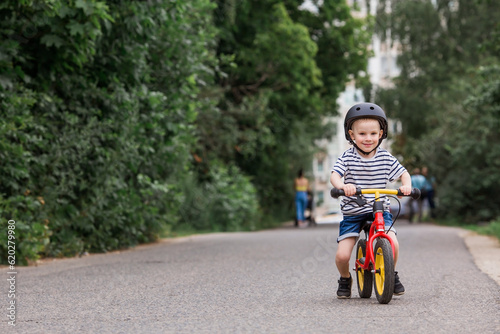 A cheerful little boy rides a running bike in a helmet outdoors. A happy child is engaged in an active sport. Protection. Life insurance and child safety. © Юлия Клюева
