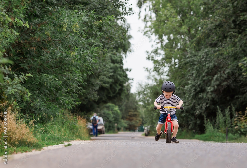 A cheerful little boy rides a running bike in a helmet outdoors. A happy child is engaged in an active sport. Protection. Life insurance and child safety. A cheerful little boy rides a running bike in a helmet outdoors. A happy child is engaged in an active sport. Protection. Life insurance and child safety.
