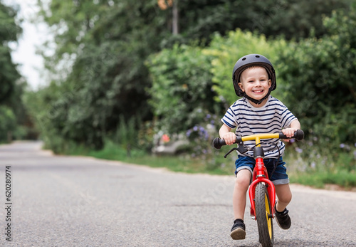 Fototapeta Naklejka Na Ścianę i Meble -  A cheerful little boy rides a running bike in a helmet outdoors. A happy child is engaged in an active sport. Protection. Life insurance and child safety.