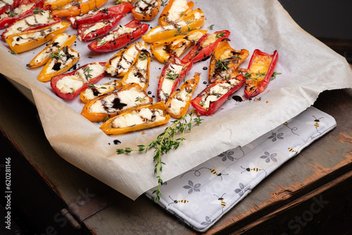 Mini peppers, halved, stuffed with goat cheese, roasted, then drizzled with hot honey and balsamic glaze, on a parchment lined baking pan.