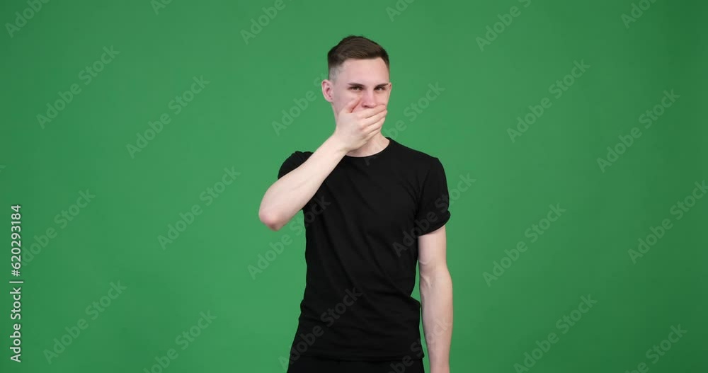 On a green background, a confident Caucasian man is shown with his hand covering his mouth. His facial expression exudes self-assurance and a sense of authority. On a green background, a confident Caucasian man is shown with his hand covering his mouth. His facial expression exudes self-assurance and a sense of authority.