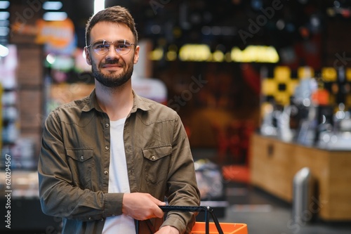 Portrait of smiling handsome man grocery shopping in supermarket, choosing food products from shelf