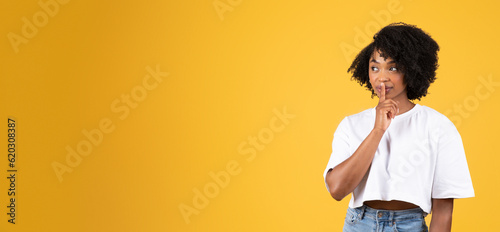 Bild auf Leinwand Positive serious young black woman in casual making shh gesture with finger