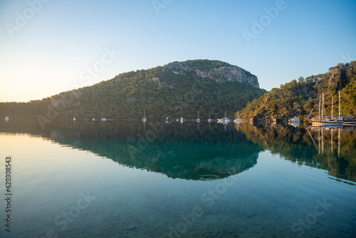 Fototapeta Naklejka Na Ścianę i Meble -  Beautiful sea coast near Cleopatra Bath Bay, Gocek, Fethie, Turkey. Landscape with moor yachts, clear blue water and pine trees in the morning.