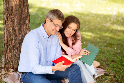 Beautiful mature couple resting at summer park, reading book together