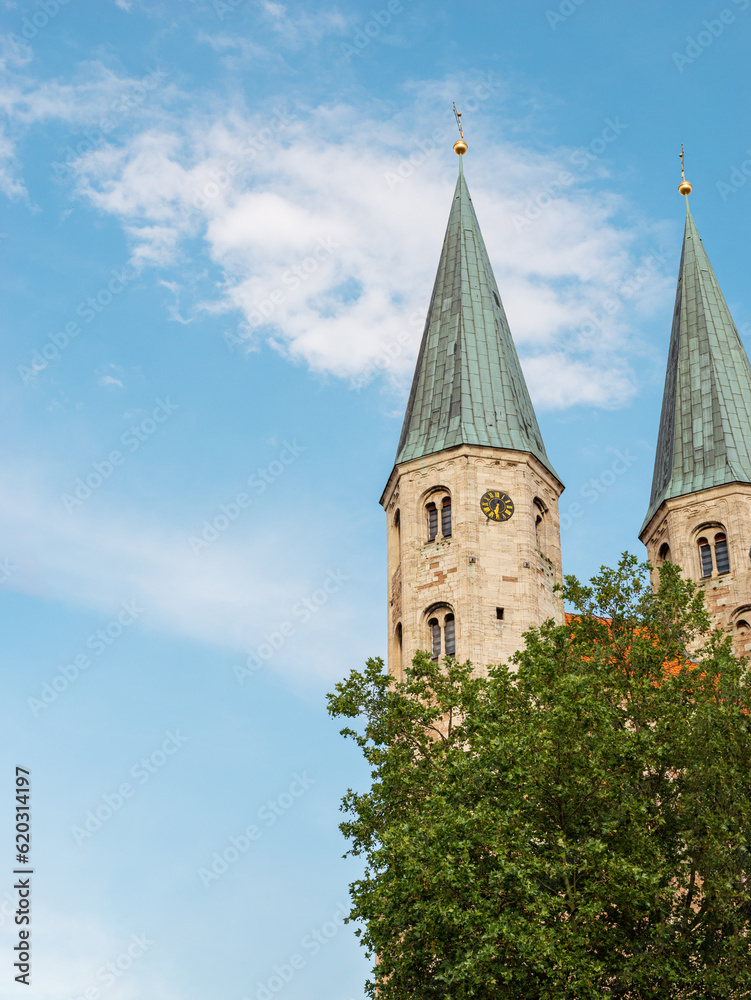 Two medieval towers of St.Martini church against the blue sky and green tree. Sights of Braunschweig, Germany. Vertical photo with elements of historical buildings.