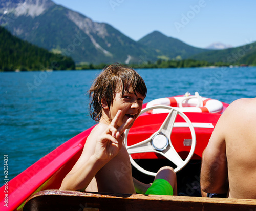 Boy on red boat on sky blue lake in summer in Tyrol, Austria 