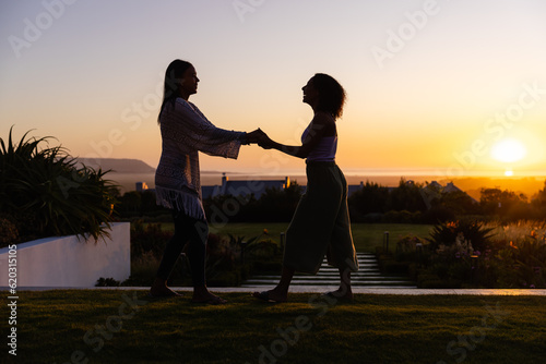 Happy biracial lesbian couple dancing in garden at sunset