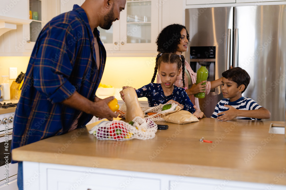 Happy biracial parents, son and daughter unpacking grocery shopping in kitchen Happy biracial parents, son and daughter unpacking grocery shopping in kitchen