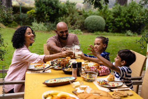 Happy biracial parents  son and daughter at table having meal making a toast in garden