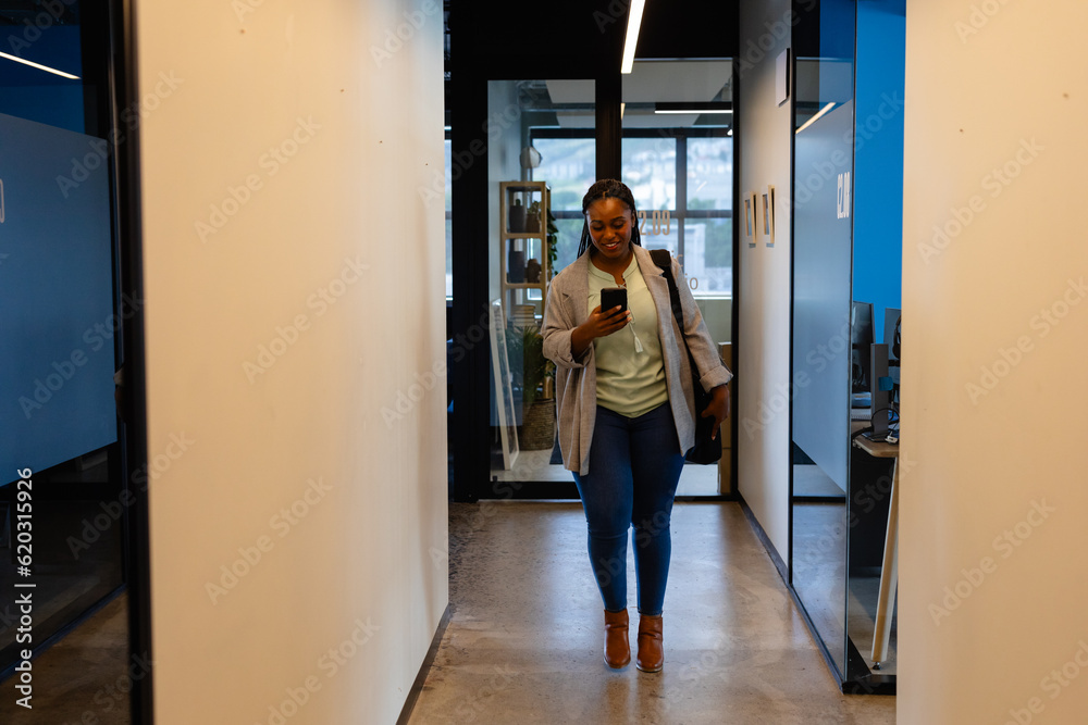 Happy plus size african american casual businesswoman using smartphone in office corridor Happy plus size african american casual businesswoman using smartphone in office corridor