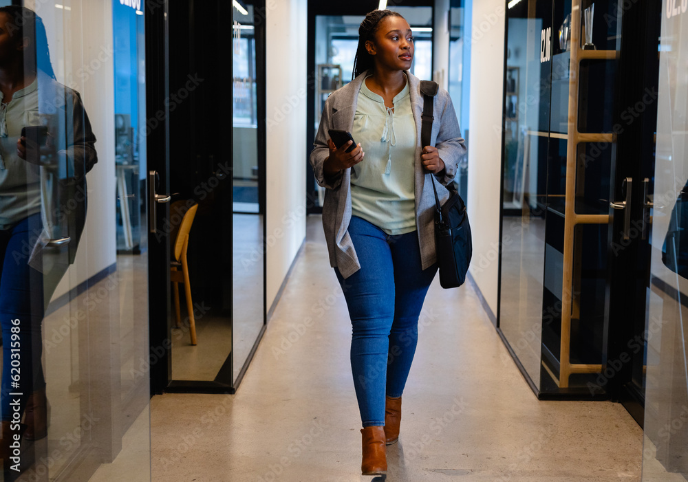 Plus size african american casual businesswoman using smartphone in office corridor