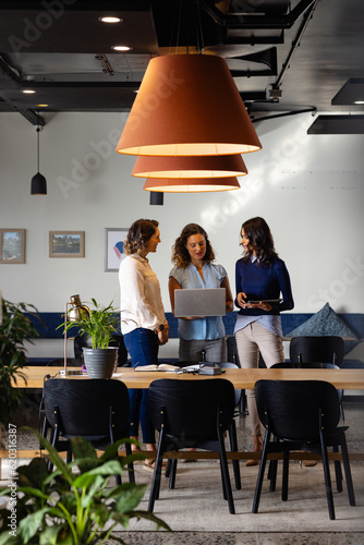 Happy diverse casual businesswomen discussing using laptop and tablet in office