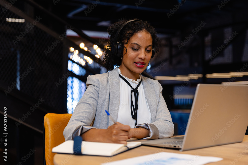 Biracial casual businesswoman with headphones making video call using laptop in office Biracial casual businesswoman with headphones making video call using laptop in office