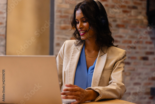 Happy middle eastern casual businesswoman with headphones making video call using laptop in office