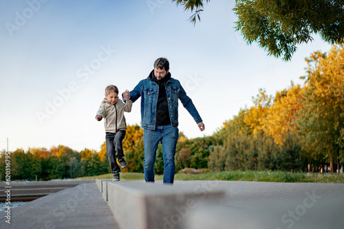 Caucasian bearded man with his little son walking in park holding hands on autumn day