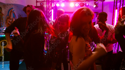 POV of happy adults enjoying disco party at club, having fun together on modern electronic music. Friends dancing and partying in discotheque, jumping under stage lights. Handheld shot.