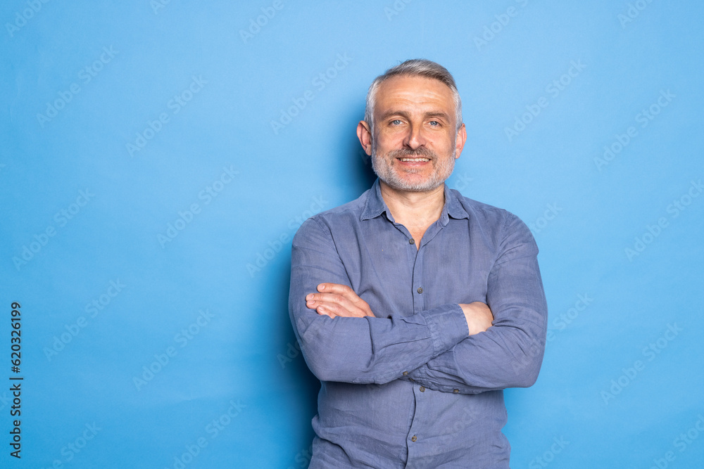 Handsome middle aged grey haired man standing with arms folded isolated on blue background. Handsome middle aged grey haired man standing with arms folded isolated on blue background.
