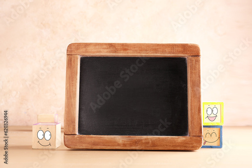 Empty chalkboard and cubes with drawn happy faces on grunge background