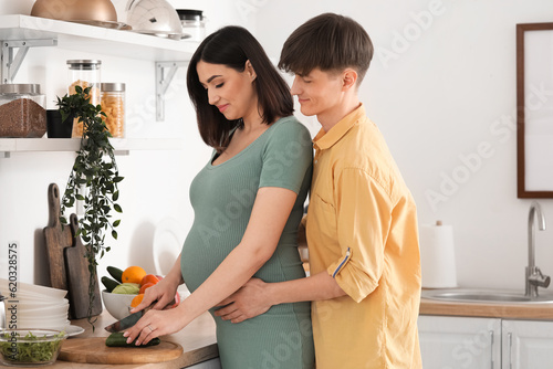 Young pregnant woman with her husband cutting cucumber in kitchen © Pixel-Shot