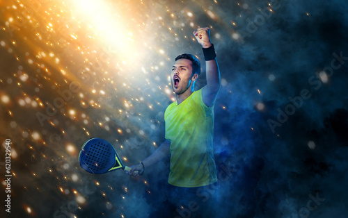 Padel tennis player celebrates victory in the game. Man athlete with paddle tenis racket on background with sparks and fire. Sport concept. Download a high quality photo for sports website.