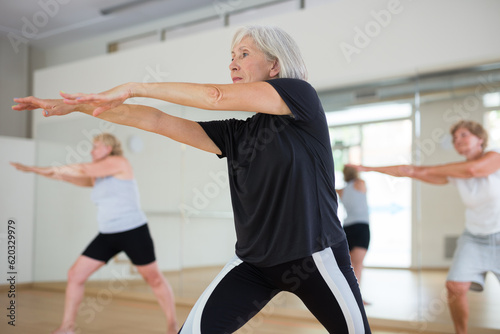 Group of three mature women performing dance in exercise room.