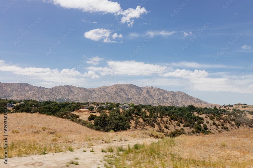 A beautiful American landscape with mountains, trees, and country houses in California on sunny days with blue sky. Bakersfield, California, USA - 7-22-2021