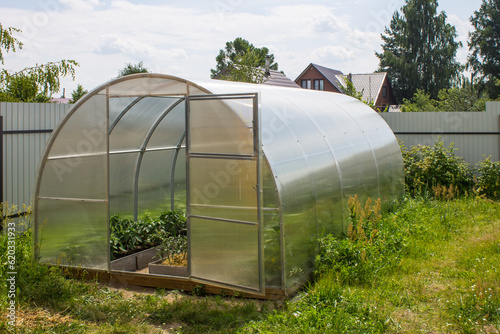 Transparent semicircular polycarbonate greenhouse close-up in the garden on a summer day